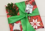 Prezent zapakowany w świąteczny papier, z zieloną kokardą, małym pudełeczkiem oraz gałązką choinki