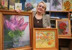 Uśmiechnięta kobieta prezentuje obrazy, na których namalowała kwiaty