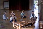 Dzieci siedzą na drewnianej podłodze i słuchają muzyki.