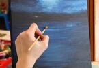 Kobieta malująca obraz. Na obrazie woda oraz księżyc za mgłą.