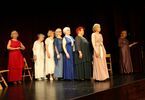 Kobiety w średnim wieku w kolorowych sukienkach stoją na scenie.
