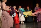 Kobiety w średnim wieku w kolorowych sukienkach tańczą na scenie.