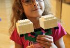 Dziewczynka trzymająca w dłoniach budowlę z klocków Lego