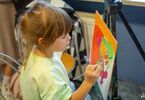 Dziewczynka malująca obraz znajdujący się na sztaludze przy użyciu pędzla