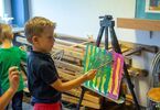 Chłopiec mieszający farby znajdujące się na płótnie, które stoi na sztaludze do malowania