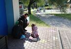 Na fotografii dziewczynka malująca kredami po chodniku, obok niej towarzyszące jej osoby dorosłe