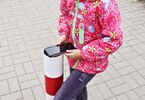 Uśmiechnięta dziewczynka oparta o słupek na chodniku, trzymająca smartfona w dłoniach
