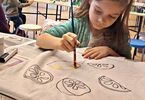 Dziewczynka malująca farbami torbę z narysowanymi owocami
