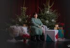 Pracownica DK Zacisze pozująca do zdjęcia na świątecznym tle w formie choinek z lampkami, prezentów, siedząca na świątecznym fotelu i pufach DK Zacisze