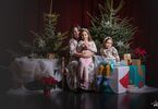 Matka z córkami pozująca do zdjęcia na świątecznym tle w formie choinek z lampkami, prezentów, siedząca na świątecznym fotelu i pufach DK Zacisze