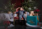 Chłopiec pozujący do zdjęcia na świątecznym tle w formie choinek z lampkami, prezentów, siedzący na świątecznym fotelu i pufach DK Zacisze