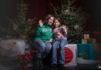 Matka z córką pozująca do zdjęcia na świątecznym tle w formie choinek z lampkami, prezentów, siedząca na świątecznym fotelu i pufach DK Zacisze