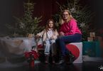 Matka z córką pozująca do zdjęcia na świątecznym tle w formie choinek z lampkami, prezentów, siedząca na świątecznym fotelu i pufach DK Zacisze