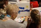 Dziadkowie z wnuczętami z okazji Dnia Babci i Dziadka malujący portrety farbami
