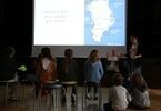 Prowadząca omawiająca Grenlandię, przed nią siedzące dzieci, patrzące na slajdy prezentacji