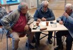Trzech starszych mężczyzn przy stoliku, rozmawiają i notują