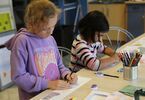 Dwie dziewczynki rysują kredkami obrazkowe opowieści