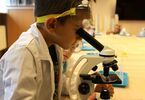 Chłopiec w białym fartuchu patrzy przez mikroskop