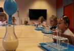 Dzieci siedzące przy stole na którym stoi szklana bańka z balonem