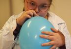 Dziewczynka w okularach dmucha niebieski balon