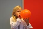 Dziecko w białym fartuchu dmucha pomarańczowy balon