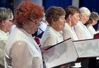 Starsze kobiety w białych bluzkach śpiewają zerkając w śpiewnik