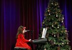 Dziewczynka w czerwonej sukience gra na pianinie elektronicznym, obok choinka