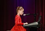 Dziewczynka w czerwonej sukience i rajstopkach  śpiewa i gra na pianinie elektronicznym