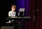 Chłopiec w marynarce gra na scenie na pianinie elektronicznym
