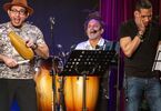 Trzech mężczyzn o latynoskiej urodzie gra na scenie na różnych instrumentach