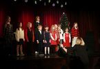 Grupa dzieci i młodzieży w świątecznych ubraniach na scenie, kobieta przed sceną gestykuluje rękoma