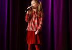 Dziewczynka w czerwonym stroju śpiewa do mikrofonu