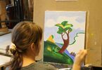 Kobieta  z włosami spiętymi w kucyk maluje pędzlem akrylowy obraz