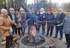 Seniorzy stoją przy ognisku i pieką kiełbaski