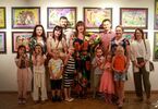 Foto grupowe, dorośli i dzieci, za nimi wystawa kolorowych prac