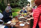 Seniorzy  siedzą przy stoach i jedzą ciasta