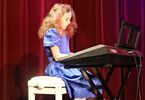 Dziewczynka w fioletowej sukience grająca na pianinie