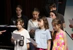 Zdjęcie: pięć dziewczyn i dwóch chłopaków z kartkami w ręce stojący obok pianina