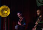 Zdjęcie: dwóch mężczyzn w średnim wieku grający na gitarach, obok lampa w żółtym kolorze, w tle bordowa kotara