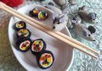 Zdjęcie: filcowe sushi w białym naczyniu, nad nimi drewniane pałeczki, z prawej strony kilka filcowych myszek,