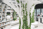 Zdjęcie: wnętrze biblioteki, widoczne białe regały z książkami, na środku pomieszczenia białe ławeczki z białymi słupami o futurystycznej architekturze, wokół nich pnące rośliny
