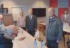 Zdjęcie sześciu osób starszych i dwóch młodszych stojących przed stołami
