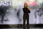 Zdjęcie: Młoda dziewczyna, w czarnym stroju, na scenie z mikrofonem, w tle napis Asteriada
