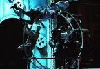 Zdjęcie: grupa osób wykonujący pokaz akrobatyczny na wielkim kole w steampunkowej scenografii w niebiesko-czarnej kolorystyce