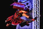 Zdjęcie: kobieta uchwycona w ruchu z walizką przy głowie w steampunkowej scenografii na tle dekoracji z wielkimi zębatkami