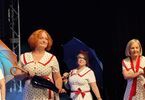 Zdjęcie: panie w dojrzałym wieku na scenie w sukienkach w kropki z kolorowymi, złożonymi parasolkami i dwie panie z otwartymi nad głowami