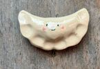 Zdjęcie: ceramiczny pierożek, w kolorze beżowym, z namalowanym uśmiechem i oczkami