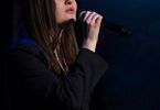 Zdjęcie: Młoda kobieta, brunetka z długimi włosami,  z mikrofonem w ręku