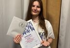 Zdjęcie: młoda kobieta, brunetka w białej koszuli, trzymająca dyplom