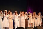 Zdjęcie: grupa osób w jasnych strojach z mikrofonami na scenie